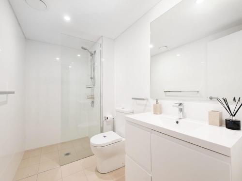 a white bathroom with a toilet and a sink at The Shoal Apartments, Unit 202/4-8 Bullecourt Street in Shoal Bay