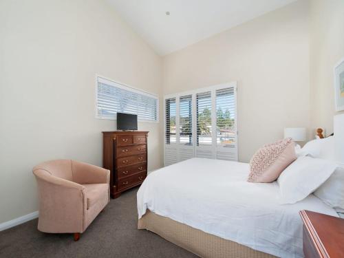 a bedroom with a bed and a chair and windows at Vogue Unit 3 197 Soldiers Point Road in Salamander Bay