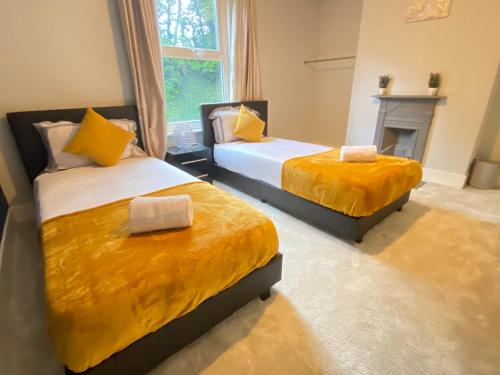 two beds with yellow sheets in a room with a fireplace at 4 Bed house sleeps 8 next to Chatham station and Chatham city centre in Chatham