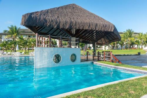 a swimming pool with a straw hut in the middle of it at Flat ou Bangalo Luxo Beach Class Beira Mar Muro Alto in Porto De Galinhas