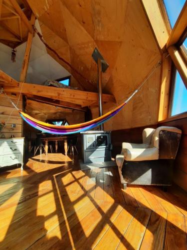 a hammock in the middle of a room with wooden floors at Domo Conguillio Conecta con tu energía sagrada junto al Salto Truful Truful con una vista majestuosa que podrás disfrutar en una tinaja Una experiencia que alineará tu espíritu y tu energía interior Vívelo in Melipeuco