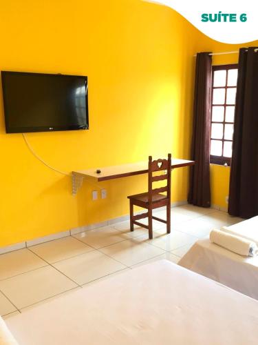 a room with a desk and a tv on a yellow wall at Suítes do Pontal in Arraial do Cabo