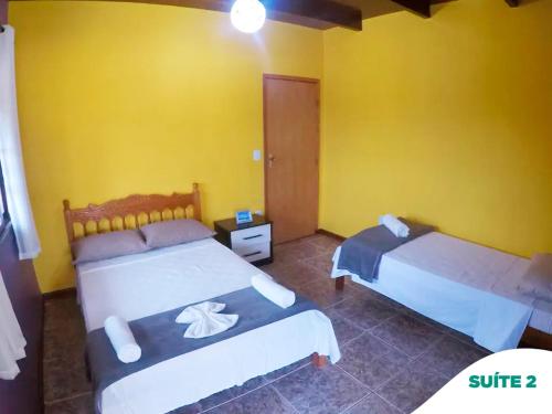 two beds in a room with yellow walls at Suítes do Pontal in Arraial do Cabo
