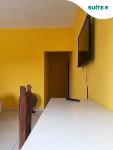 a room with a table and a tv on a yellow wall at Suítes do Pontal in Arraial do Cabo