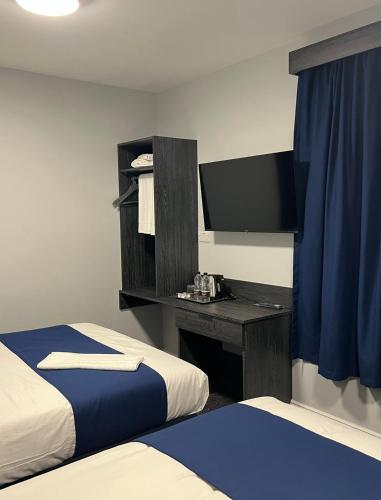 a bedroom with two beds and a desk with a television at Blue Sapphire Hotel in Ilford