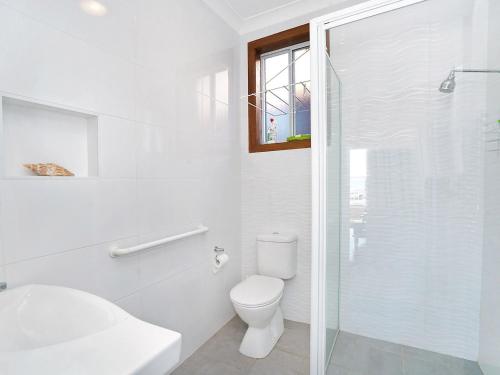 a white bathroom with a toilet and a glass shower at Beachcomer 1 in The Entrance