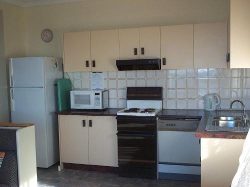 a small kitchen with white cabinets and a white refrigerator at Calypso, Unit 1 - The Entrance, NSW in The Entrance