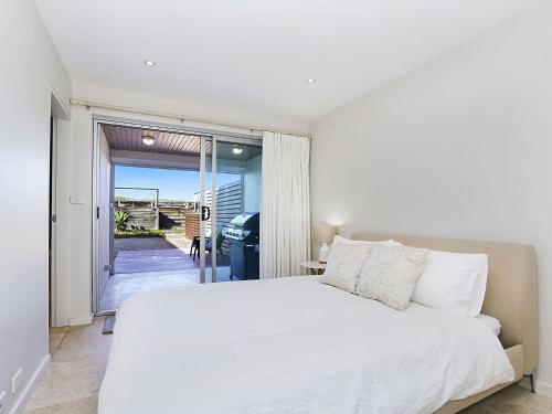 a bedroom with a white bed and a sliding glass door at Perfect Beach Front Duplex - The Entrance North in The Entrance
