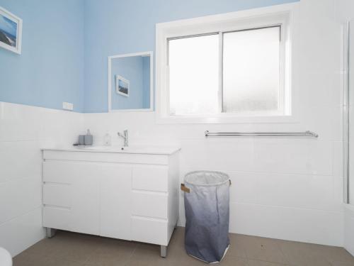 ein weißes Bad mit einem Waschbecken und einem Fenster in der Unterkunft Eloora House Blue bay in Long Jetty