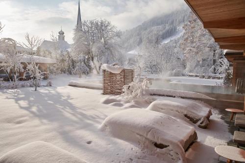 a yard covered in snow with a church in the background at MalisGarten Green Spa Hotel - Adults Only in Zell am Ziller