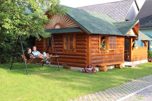 two people sitting on a swing in front of a cabin at Penzión Anna in Zuberec