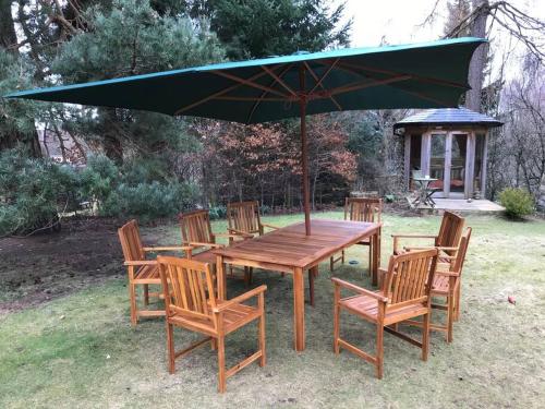 a wooden table and chairs with a green umbrella at The Beeches Studio, Highlands of Scotland in Newtonmore