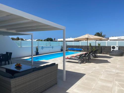 una piscina con sombrilla, mesas y sillas en Villa Ashdene - luxury modern villa with large heated pool wifi uk tv bar & BBQ en Playa Blanca