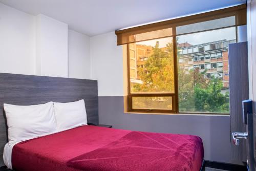 a bedroom with a bed with a red blanket and a window at Hotel Express 53 in Bogotá