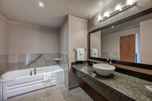 a bathroom with a tub and a sink and a mirror at Perth Parkside Hotel and Spa, BW Premier Collection in Perth