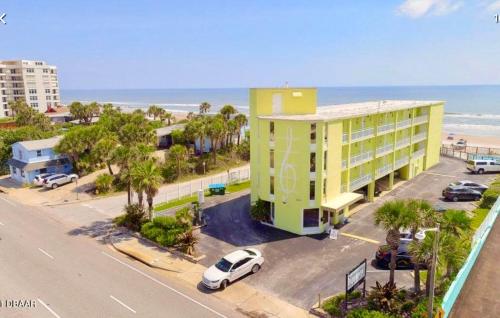 a building with a car parked in a parking lot next to the beach at Coastal Sands - Ocean View at Symphony Beach Club! in Ormond Beach