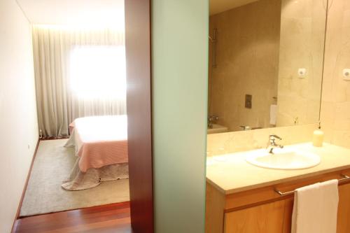 ein Bad mit einem Waschbecken, einem Spiegel und einem Bett in der Unterkunft Panoramic City View Apartment - Guimarães in Guimarães