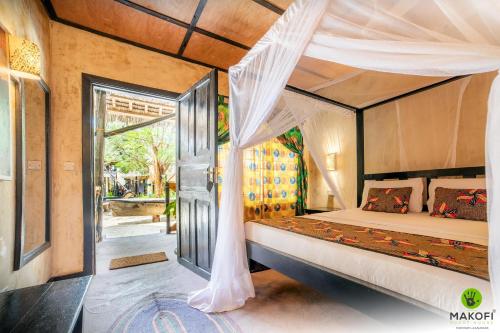 a bedroom with a canopy bed and a sliding glass door at Makofi Guest House in Nungwi