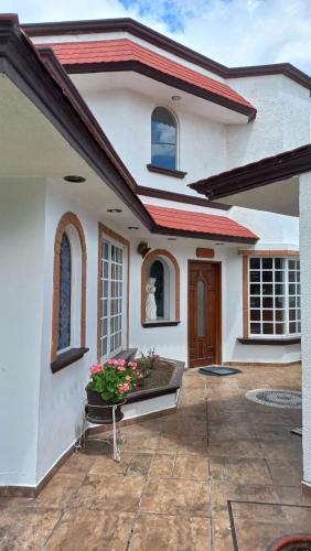 a white house with a porch with a bench and flowers at La Aurora Hotel Like Home in Huamantla