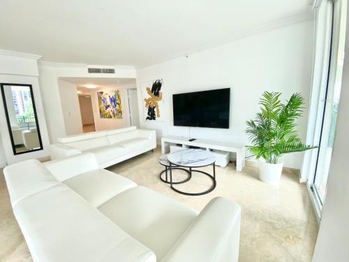 a white living room with white furniture and a flat screen tv at The King David Condos in Miami Beach