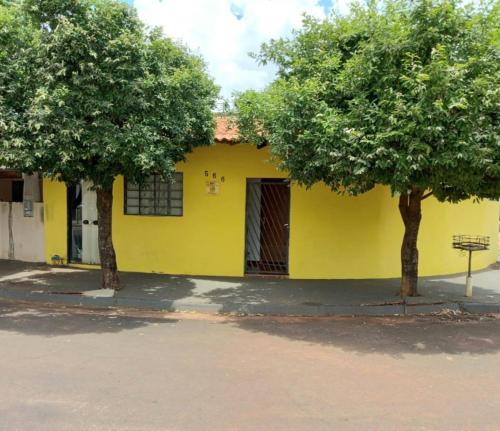 una casa amarilla con dos árboles delante de ella en Casa de temporada da Ivalda, en Olímpia