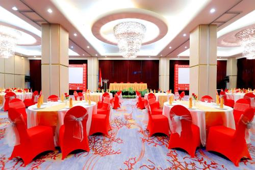 a banquet hall with red chairs and tables and chandeliers at Swiss-Belhotel Ambon in Ambon