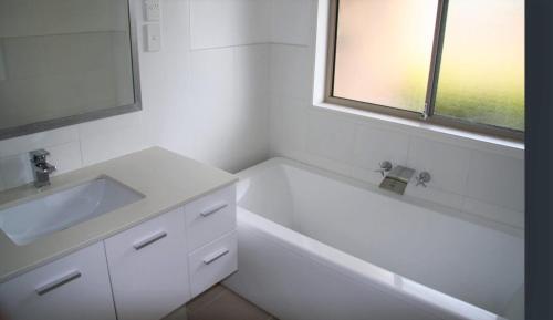 a white bathroom with a sink and a bath tub at Jarrah by Kingscliff Accommodation in Kingscliff