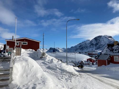 uma rua coberta de neve com uma montanha ao fundo em Isi4u apartments, snowmobile and dogsled em Sisimiut