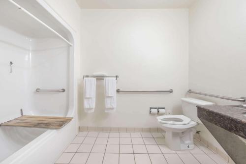 a white bathroom with a toilet and a bath tub at Super 8 by Wyndham Fort Worth Downtown South in Fort Worth
