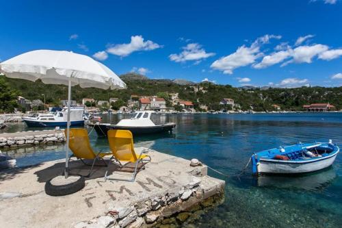two chairs and an umbrella and a boat in the water at Holiday Home Magazin in Slano