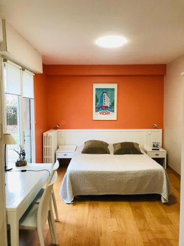 - une chambre avec un mur orange, un lit et un bureau dans l'établissement Le Clos Fleuri - Maison Vigier, à Maringues