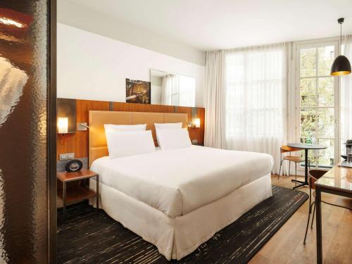 a bedroom with a large white bed and a table at Hôtel Paris Bastille Boutet - MGallery in Paris