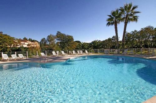 a large swimming pool with chairs and palm trees at Résidence standing Rivièra Golf Mandelieu in Mandelieu-La Napoule