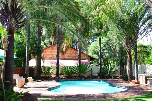 a swimming pool in a yard with palm trees at De la Rose Guesthouse in Lephalale