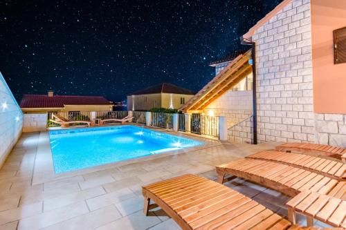a swimming pool with benches on a patio at night at Holiday Home Villa Frančeska in Postira