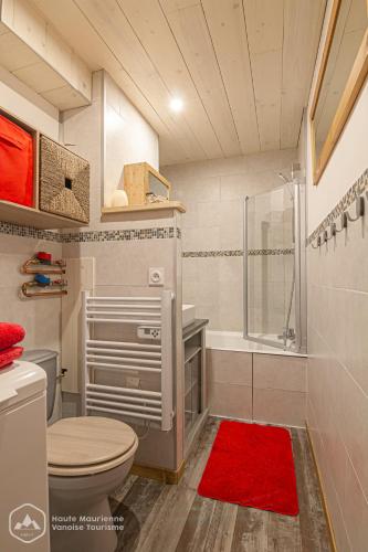 La salle de bains est pourvue de toilettes, d'une douche et d'un tapis rouge. dans l'établissement Le Cocon de l'Arcelle, à Lanslevillard