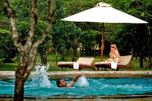 a man and woman in a swimming pool with an umbrella at Karen Blixen Camp Masai Mara in Narok