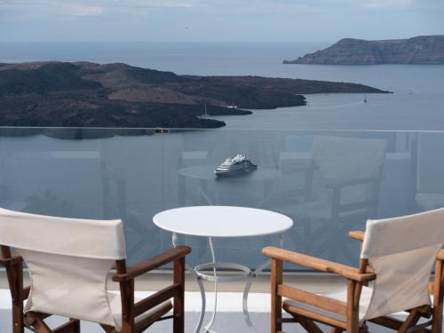 a table and chairs with a boat in the water at NEOKLASSIKO KOUKOULI in Fira