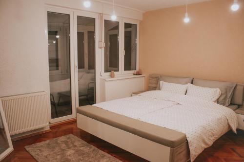 a bedroom with a bed with white sheets and windows at Take it easy Apartment in Visoko
