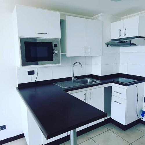 a white kitchen with a sink and a microwave at Departamento NEO IQUIQUE VISTA AL MAR 3 in Iquique