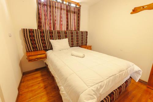 a small bedroom with a white bed with a window at Los Ponchos Inn Apartasuite in Otavalo