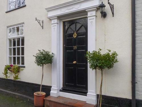 a black door on a white house with two plants at Ted's Place in Aylsham