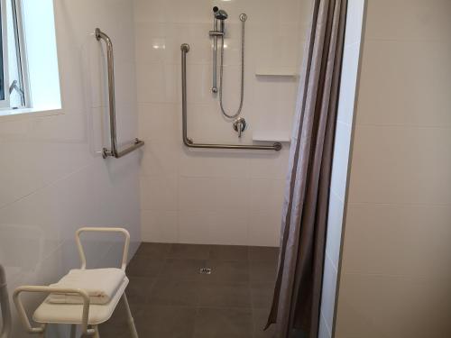 a bathroom with a shower with a chair and a shower curtain at Airport Palms Motel in Christchurch
