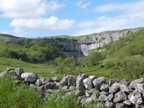 a rock wall in a field with a mountain in the background at The Snug in Keighley