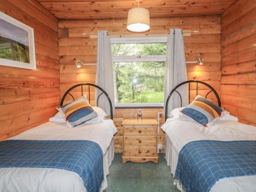 two beds in a log cabin with a window at Otter Lodge in Strathpeffer