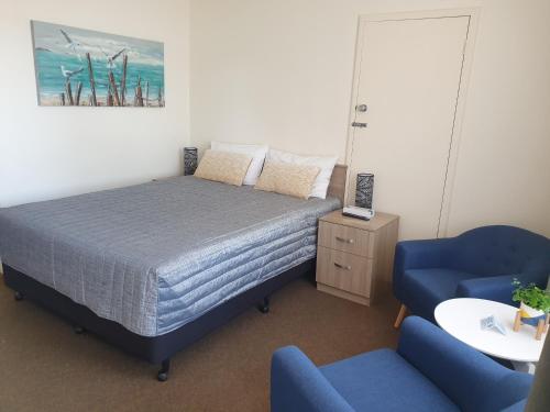 a bedroom with a bed and two blue chairs at Sandpiper Motel Ulladulla in Ulladulla