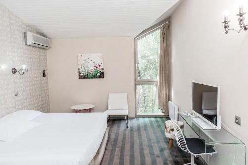 a white bedroom with a bed and a tv and a window at Hôtel Restaurant du Château de la Tour in Béguey