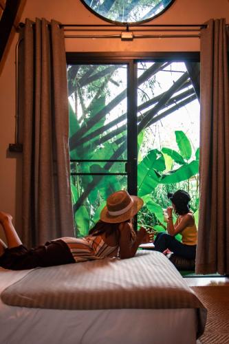 a woman laying on a bed looking out a window at เข้าค่าย Cafe & Resort - Pet Friendly in Khao Kho