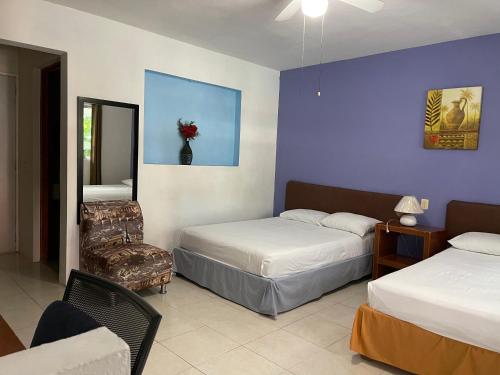 a bedroom with two beds and a chair and a mirror at Hotel Villa Escondida Campeche in Campeche