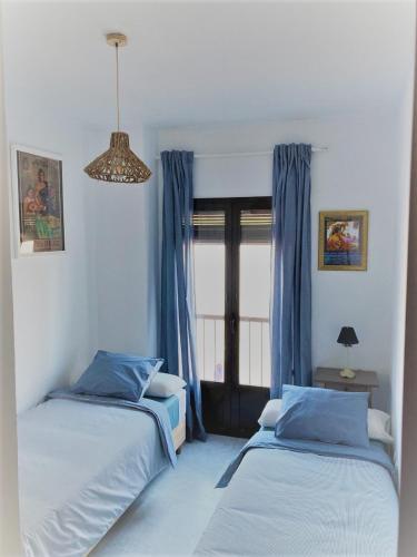 two beds in a room with blue curtains and a window at El Envero Apartamento in Jerez de la Frontera